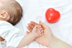 adulto segurando mão de bebê com coração